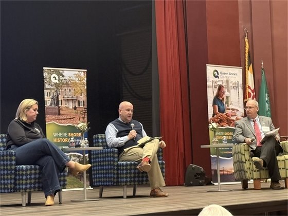 two men and a woman sitting in chairs on a stage