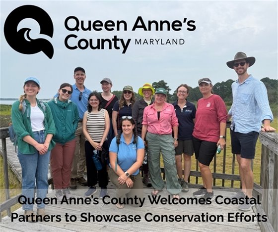 group of people standing on a wooden deck. All are smiling and wearing outdoor / hiking clothing