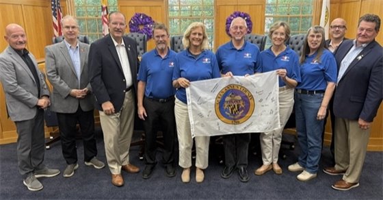 Groups of people standing in a line holding a flag with the queen annes county seal on it.