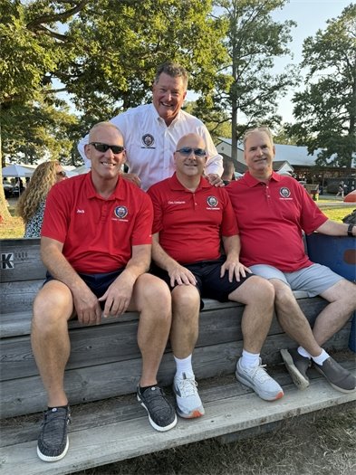 three men in red shirts sitting on a trailer with a man with a white shirt standing behind them all are smiling