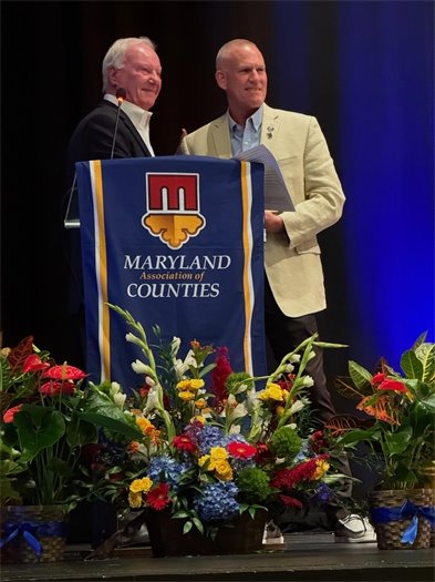 two men standing behind a podium with flowers in front