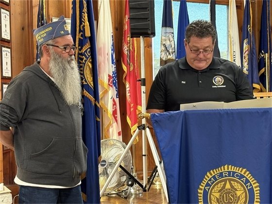 Two men standing behind a podium, one is wearing glasses and reading